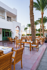 Outdoor dining area with wooden tables and palm trees at a resort during blue hour in a warm climate