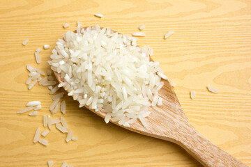 A wooden spoon filled with uncooked rice on a wooden plank background. © daniel limantara