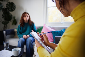 Female psychiatrist making notes during therapy session of young woman