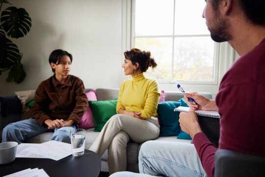 Father making notes while his son talking with psychotherapist in office