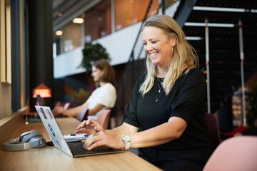 Smiling blond businesswoman working on laptop at desk in office