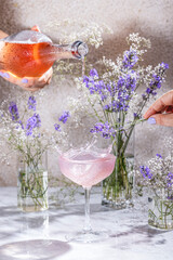 Obraz premium Bartender pouring pink drink into coupe glass with lavender garnish and flowers