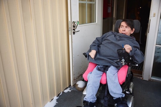 High angle view of mature man with cerebral palsy sitting on wheelchair wheeling through door of nursing home