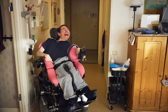 Full length of cheerful mature man with cerebral palsy sitting on motorized wheelchair in nursing home