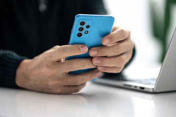 Closeup image of a male hands using smartphone and laptop. Boy working online, internet applications