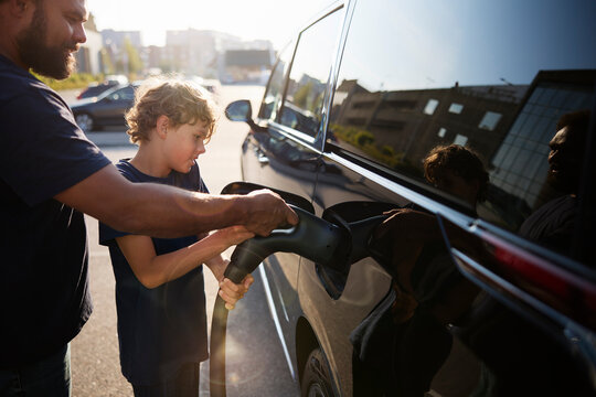 Father assisting son charging electric car at street