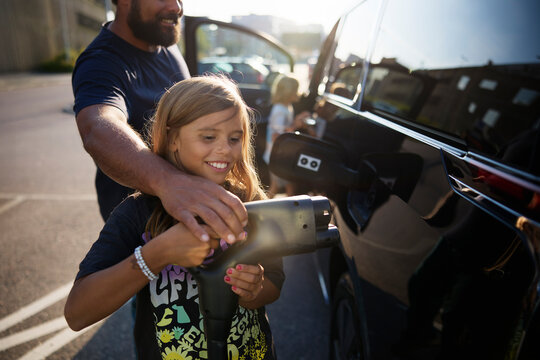 Smiling girl holding electric plug with father near car at street