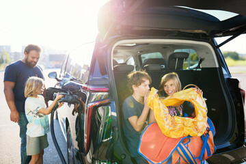 Siblings blowing inflatable ring while father assisting son charging car at street on sunny day
