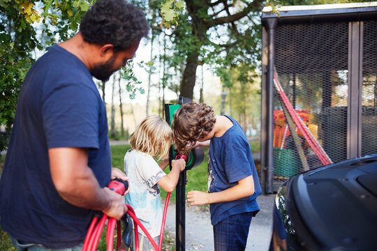 Brothers plugging electric plug in electrical outlet at charging station on street