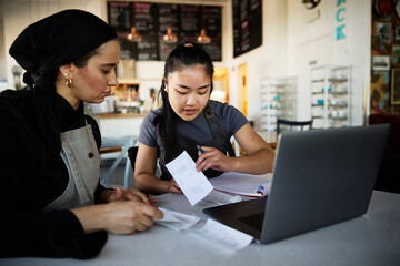 Female cafe worker helping manager in sorting out financial bills at coffee shop