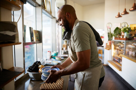 Side view of male owner holding stack of plates while working at cafe