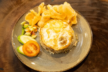 A plate of fried rice with a fried egg on top, served on a beautifully designed plate, placed on a wooden table for a warm and appetizing presentation