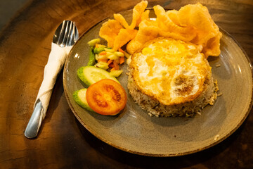A plate of fried rice with a fried egg on top, served on an elegant plate with a spoon and fork, placed on a wooden table for a warm and inviting dining presentation