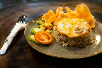 A plate of fried rice with a fried egg on top, served on an elegant plate with a spoon and fork, placed on a wooden table for a warm and inviting dining presentation