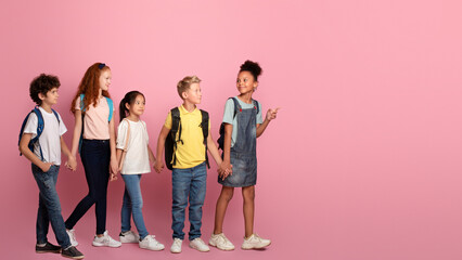 Body size portrait of schoolkids walking to school hand in hand on pink background