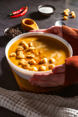Woman holding bowl of pumkin soup with rusks. Served table with cream soup, chili pepper and napkin. Vegetable soup flat lay