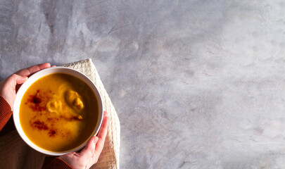 Woman holding bowl of pumpkin soup with paprika spices and cream on white table. Kitchen napkin....
