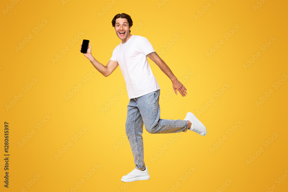 Leinwandbilder happy young man showing empty smartphone screen while jumping up over yellow studio background, full