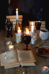 Books, lit candles, red wine, snacks and various deocration on the table. Dark academia or Halloween concept. Selective focus.