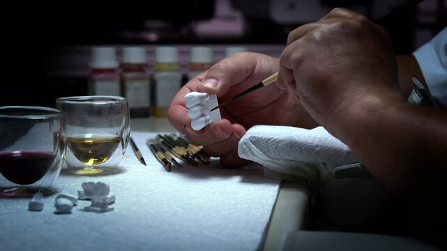 A dental technologist paints partial dentures to mimic the look of real teeth.