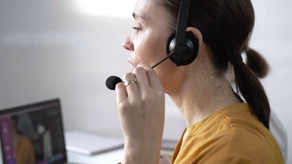 Focused female call center operator in yellow casual blouse is assisting clients online, providing customer support and answering inquiries. Call center concept
