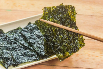 chopsticks picking up nori seaweed in a plate on a wooden table