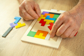 male hand manipulates colorful wooden puzzle, elderly old man composing geometric shapes, brain health and mental well-being, preventing dementia and Alzheimer's disease