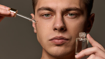 Close-up of man applying serum under eye with dropper, liquid running down cheek, focused...