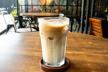 A refreshing iced latte in a clear glass, placed on a wooden table inside a cozy café, creating a warm and inviting coffee shop atmosphere