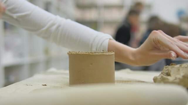 A close-up of a pottery masterclass where a participant skillfully shapes a clay mug by hand learning the art of ceramics. In the background, a group of people are also engaged in pottery