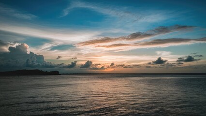 Serene sunset panorama with blended blue and orange hues, lush clouds above calm water, capturing summer evening tranquility and beauty