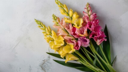 Beautiful top view of a vibrant bouquet with yellow and pink gladiolus flowers against a light textured background showcasing lush green leaves.