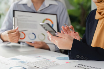 Diverse professionals analyzing financial reports and using a smartphone for strategy planning in the office.