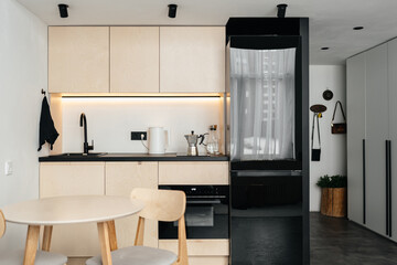 Stylish kitchen design made of plywood in beige with white walls, black glass refrigerator, stove.