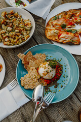 A vibrant Mediterranean meal at a seaside restaurant in Fethiye, Türkiye. Featuring fresh burrata, crispy zucchini chips, artisanal bread, and smoked salmon pizza on a rustic wooden table