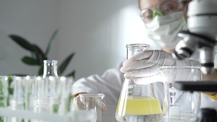 Woman scientist researcher wearing white protective gloves is shaking up a yellow chemical solution...