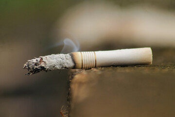 Lit white cigarette with smoke coming out of it sitting on the grey city concrete with copy space	
