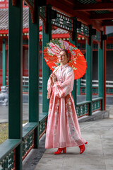 Naklejka premium Portrait of a young Asian woman in a pink kimono and an umbrella in her hand in the park. Chinese New Year