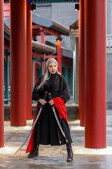 A warrior girl in a Chinese costume practices wushu kung fu with weapons in an open area. National...