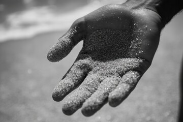 A person stands on the beach, holding sand in their hand