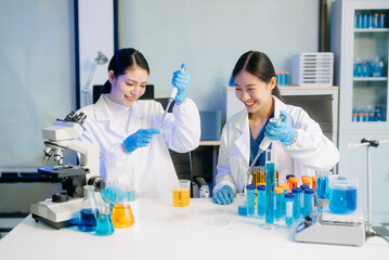 Fototapeta premium Two Asian female scientists in a high-tech lab analyzing biochemical samples, using micro pipettes,