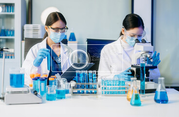 Two Asian female scientists conduct biochemical research using micro pipettes in a high-tech...