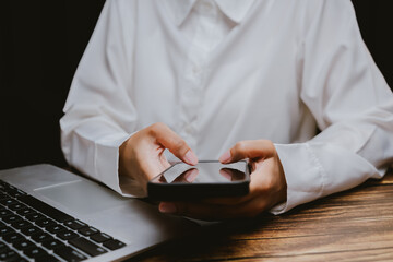 Hands Holding Smartphone Next to Laptop on Wooden Desk