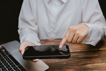 Person Using Smartphone While Working on Laptop at Wooden Desk