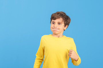 Young boy with clenched fist and expression of despair, fed up with a situation, misunderstood and desperate, in yellow sweater, isolated on blue background