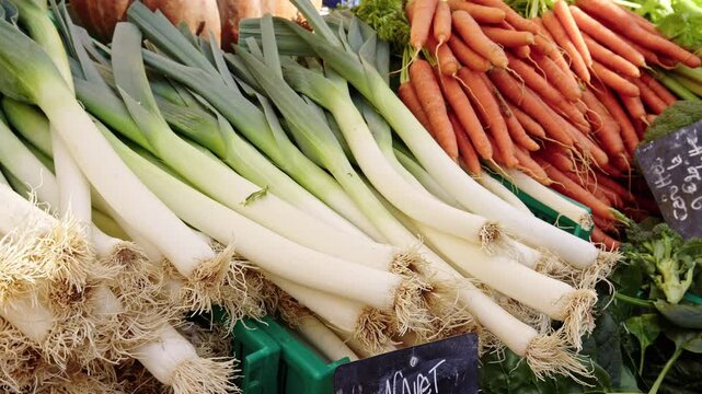 Colorful leeks and vibrant carrots are displayed at a bustling farmer's market. Local farmers showcase their produce to eager shoppers. The atmosphere is lively and inviting.