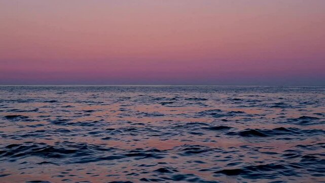 Time-lapse wide shot reveals the tide&rsquo;s rhythmic movement under a pastel-hued sunrise, soft pinks and oranges reflecting on gentle swells.
