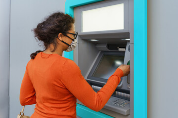 Black woman wearing protective mask while withdrawing money at ATM.