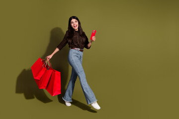 Portrait of a stylish young woman holding red shopping bags and smartphone against khaki background