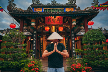 male tourist in a Vietnamese Non La hat prays at a temple on a Buddhist pagoda in Hoi An in Vietnam...